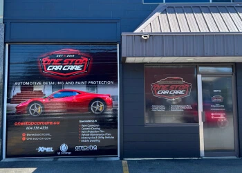 Exterior of One Stop Car Care with a large garage window graphic displaying a red sports car, the company logo, contact info, and listed services such as detailing and paint protection.