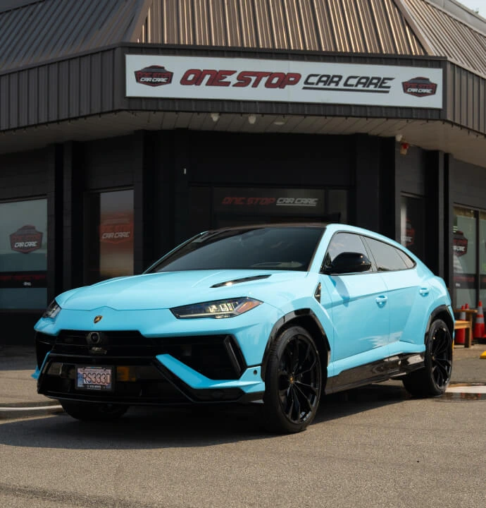 Sky blue Lamborghini Urus parked in front of the One Stop Car Care building, featuring a glossy finish, black accents, and tinted windows.