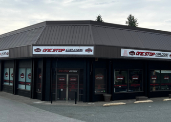 Exterior view of the One Stop Car Care building with dark walls, large logo signage around the roofline, and window decals displaying the company branding.