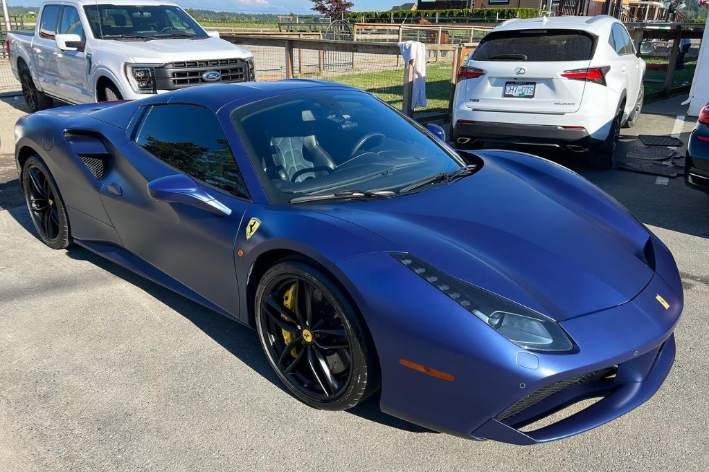 A matte blue Ferrari parked in a sunny lot with a sleek, smooth finish, showing minimal reflection—highlighting the understated appeal of a ceramic-coated satin or matte paint surface.