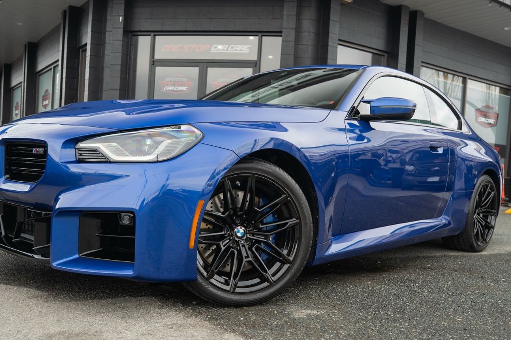 A glossy blue BMW coupe with black wheels parked outside One Stop Car Care, showcasing a freshly applied ceramic coating that enhances its vibrant paint and mirror-like reflection.
