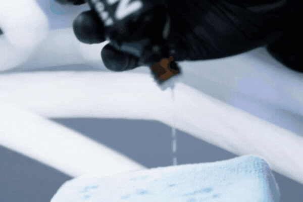 Close-up GIF of a gloved hand pouring ceramic coating liquid from a small bottle onto a blue microfiber applicator pad, showing the product’s smooth and controlled application process.