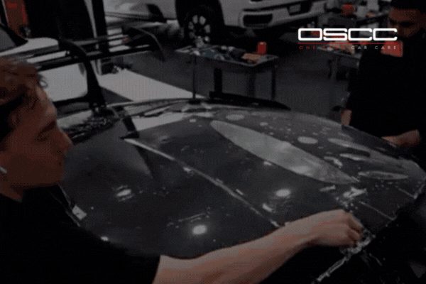 Two technicians at a Surrey auto shop apply paint protection film to a black car hood, showing what is PPF and how it shields vehicles from road debris and harsh weather.