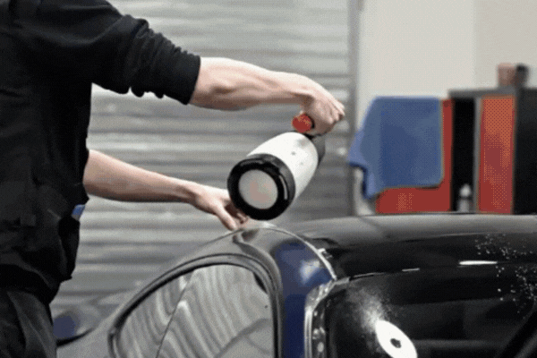 A technician sprays liquid solution onto a black car’s surface in a Surrey shop, preparing the paint for paint protection film installation and helping drivers with understanding PPF benefits.