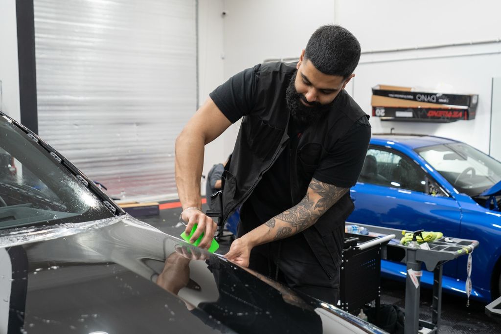 A technician in Surrey carefully applies paint protection film to the hood of a black car, illustrating what is PPF and why professional installation ensures smooth, long-lasting results.