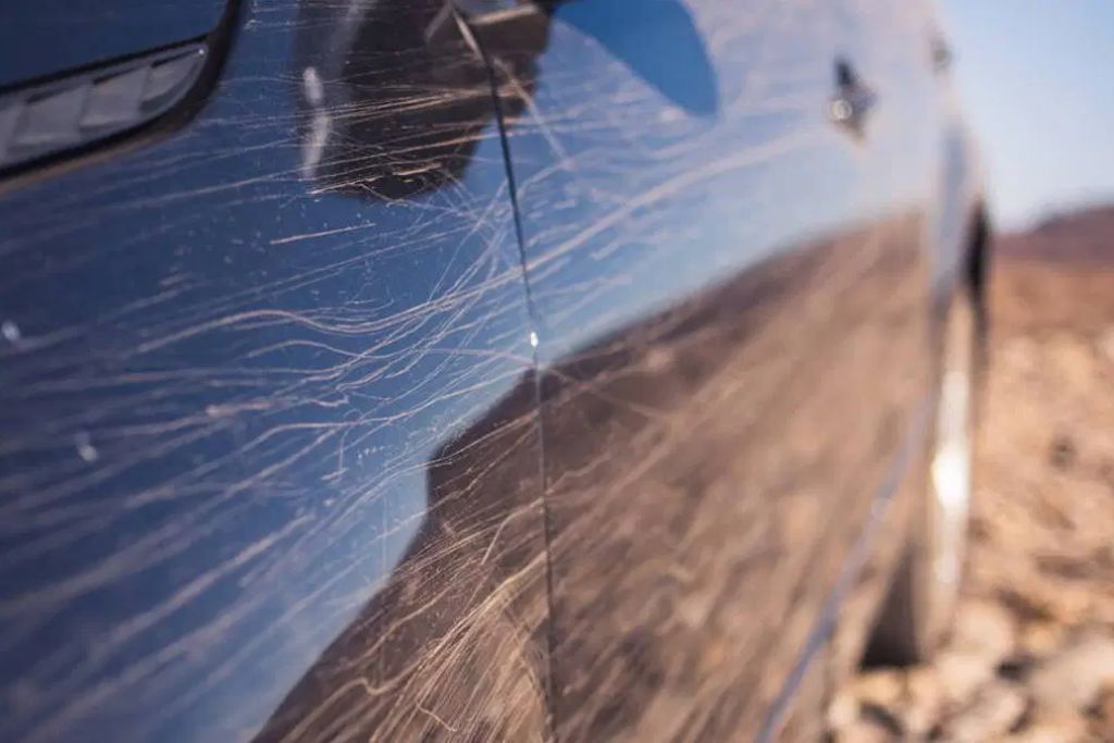 Close-up of a black car door showing numerous fine scratches and swirl marks across the surface, highlighting the limitations of ceramic coating when it comes to physical impact protection. This image is used to explain what is ceramic coating and what it can and cannot do for Surrey drivers.