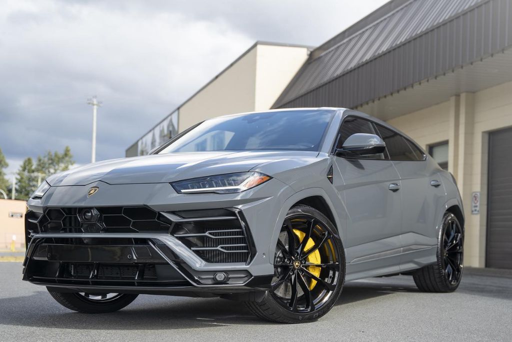 A sleek grey Lamborghini Urus with black and yellow wheels gleams under natural light outside a detailing shop, showcasing a flawless, reflective finish. This image represents the end result of professional ceramic coating, highlighting what is ceramic coating and its value for Surrey drivers.
