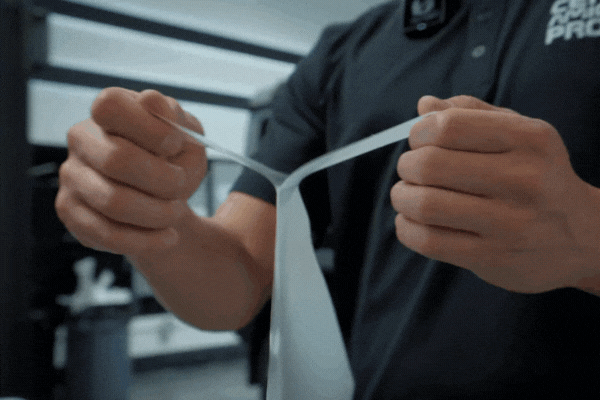 Close-up of a One Stop Car Care technician stretching a clear sheet of paint protection film in the detailing shop, demonstrating the strength and flexibility of PPF for car surface protection in Surrey.