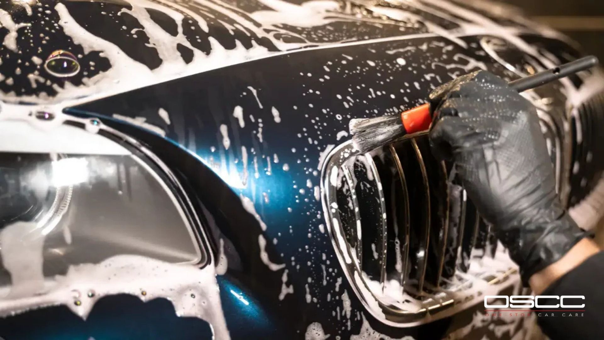 A close-up of a white melamine sponge held over a purple microfiber towel, used for delicate surfaces in car detailing.