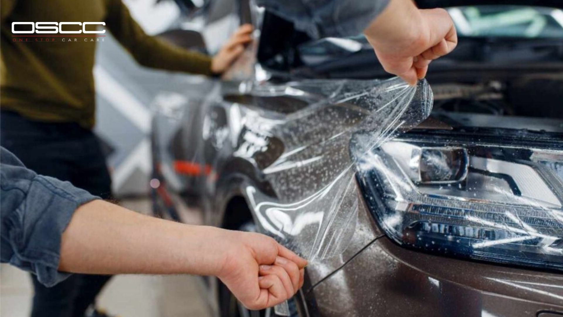 Two technicians install a transparent paint protection film on the headlight and fender area of a brown SUV, stretching and smoothing the film.