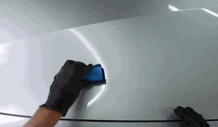 Gloved hand spreading ceramic coating evenly over a car hood using a microfiber applicator to enhance surface protection.