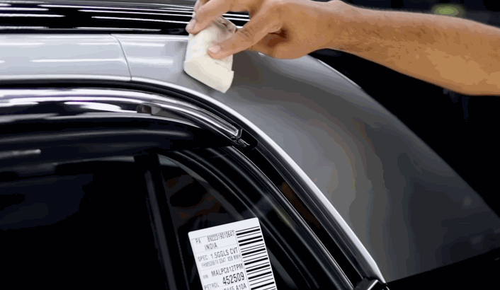 Hand applying ceramic coating along the roofline of a car using a white applicator pad to create a chemical-resistant layer.