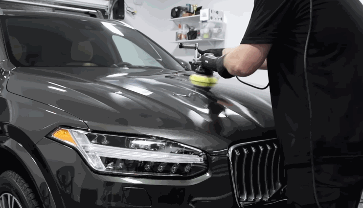 A technician uses a polishing machine on a black SUV hood to remove ceramic coating and correct surface imperfections.