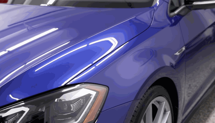A deep blue car hood reflecting bright lights as the ceramic coating is gradually removed, revealing a smooth, polished finish.