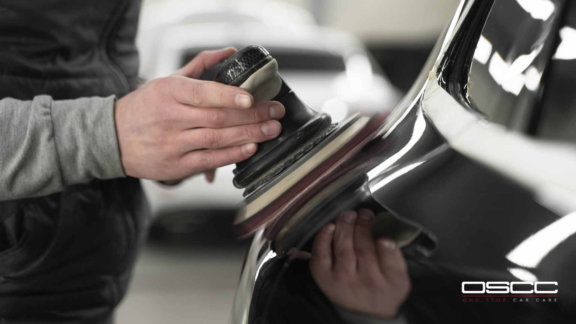 Close-up of a technician holding a dual-action polisher to remove ceramic coating from a vehicle's curved surface. The OSCC One Stop Car Care logo appears in the corner.