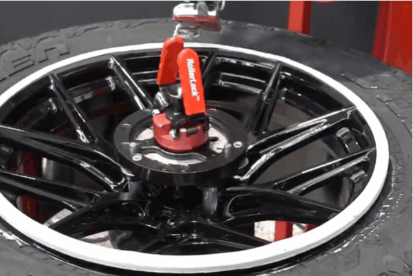 Close up of a glossy black alloy wheel mounted on a tire machine with a red torque tool securing the center hub during installation. The image highlights professional wheel installation services in Surrey to ensure precise fitment and long term performance.