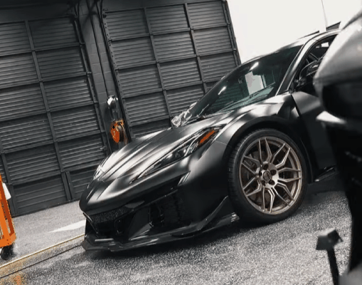 Alt text: Black sports car parked in a detailing bay with a low front splitter, sculpted hood, and bronze wheels. The sharp curves and glossy finish show why higher quality paint protection film and careful installation can affect total cost.