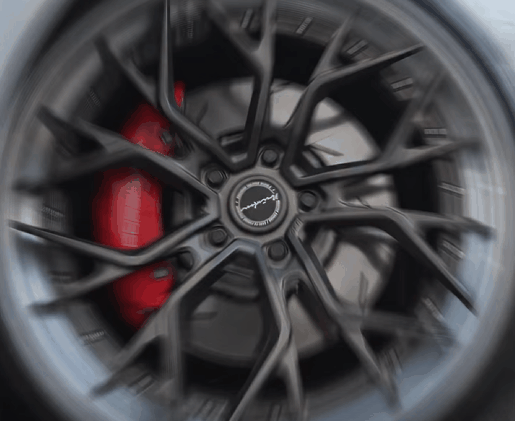 Alt text: Close up of a dark multi spoke rim with a red brake caliper visible behind it, photographed with slight motion blur to emphasize performance styling. In the rims vs tires discussion, this kind of custom wheel upgrade highlights appearance and sporty design, while tires usually have the bigger impact on grip comfort and braking.