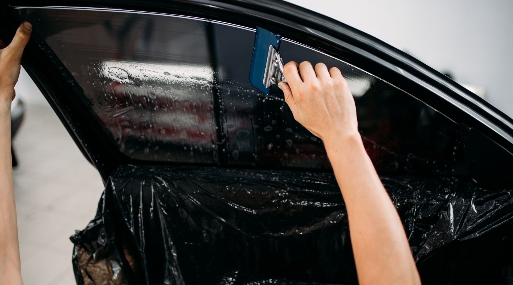 Technician applying window tint film to a car door window during professional installation