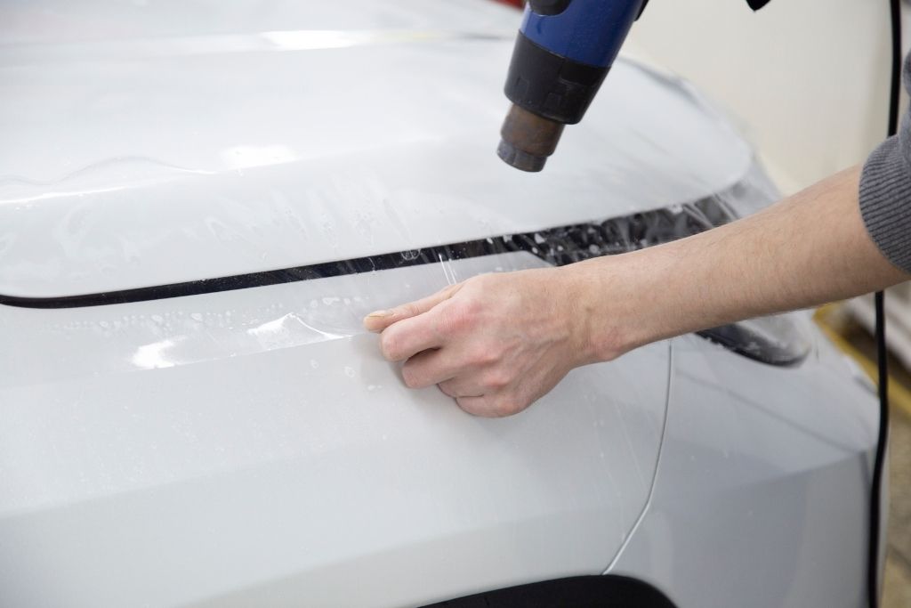Heat gun being used during paint protection film installation on a car panel to ensure smooth adhesion and finish