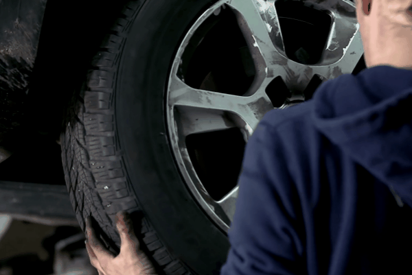 Technician handling tire during wheel installation on vehicle, highlighting professional rim and tire mounting process