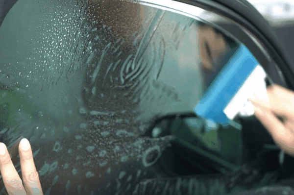 Close-up of window tint film being smoothed onto a car window during installation