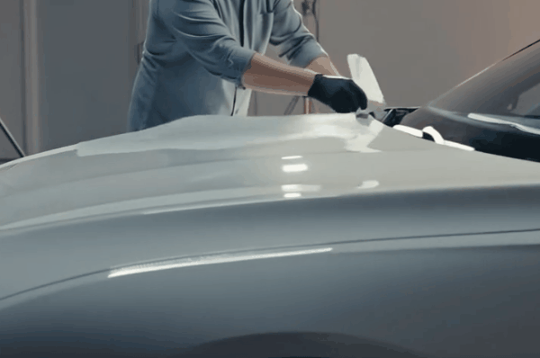 Technician applying paint protection film on a car hood to protect new vehicle paint from scratches and road damage