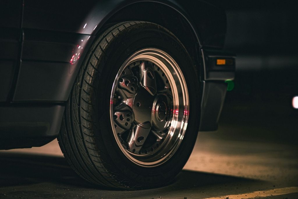 Close-up of a car tire with visible tread and polished custom rim in low lighting.