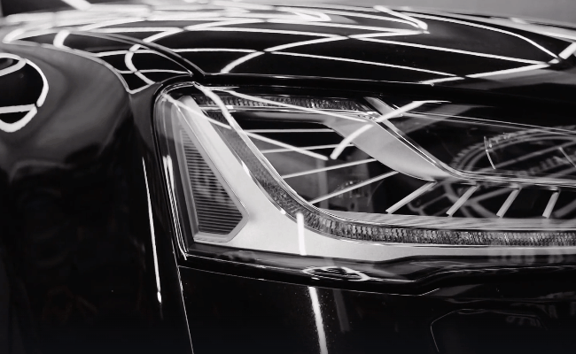 Close-up of a polished black car headlight and glossy paint finish after professional detailing.