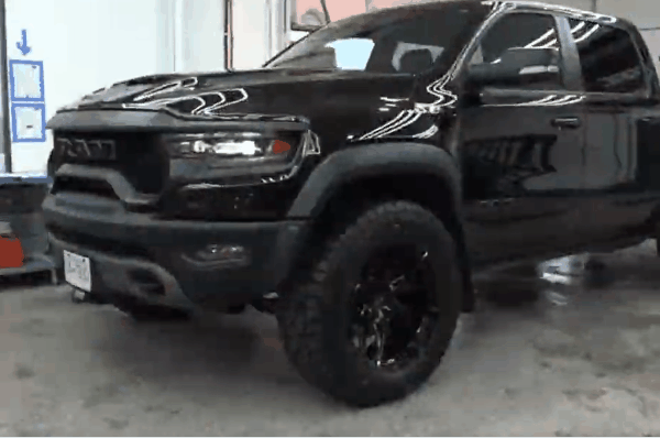 Black lifted pickup truck with large off-road tires and black rims inside One Stop Car Care shop.