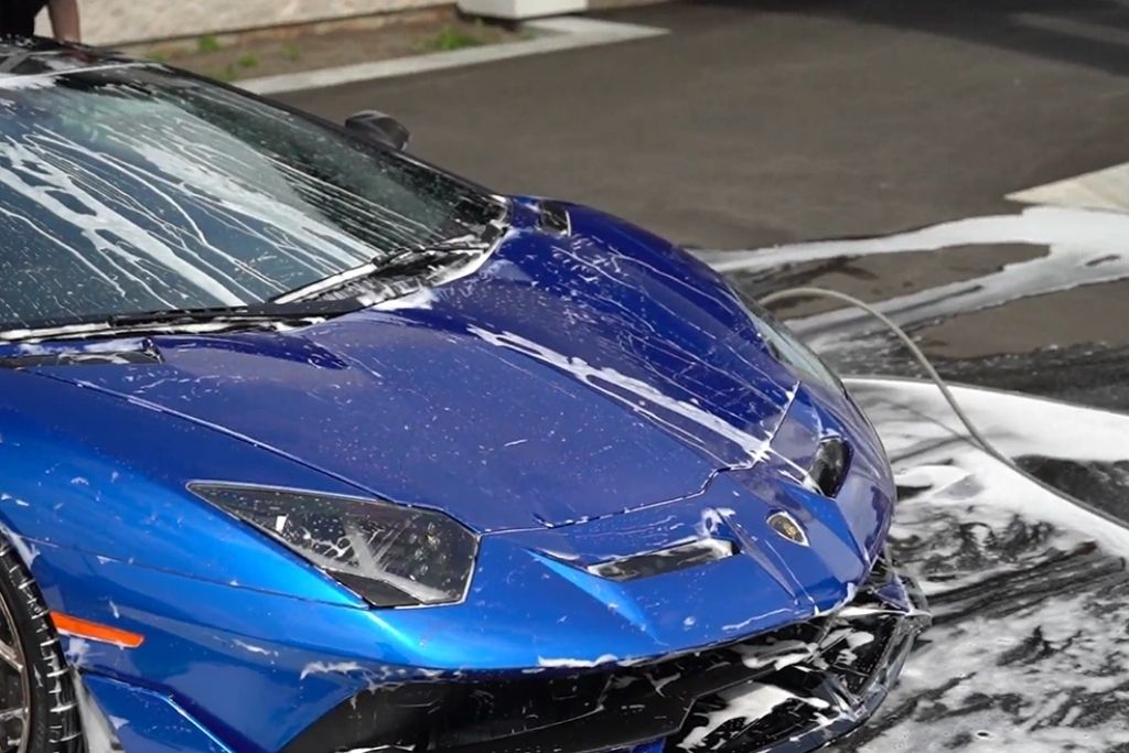 Blue sports car covered in soap during a professional exterior detailing wash.
