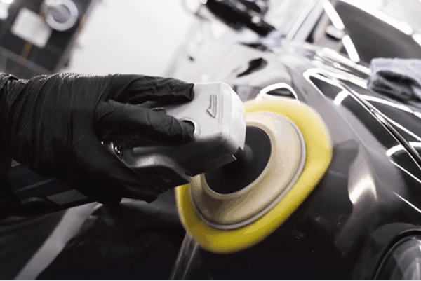 Detailing technician using a polishing machine to correct and restore a vehicle’s black paint.