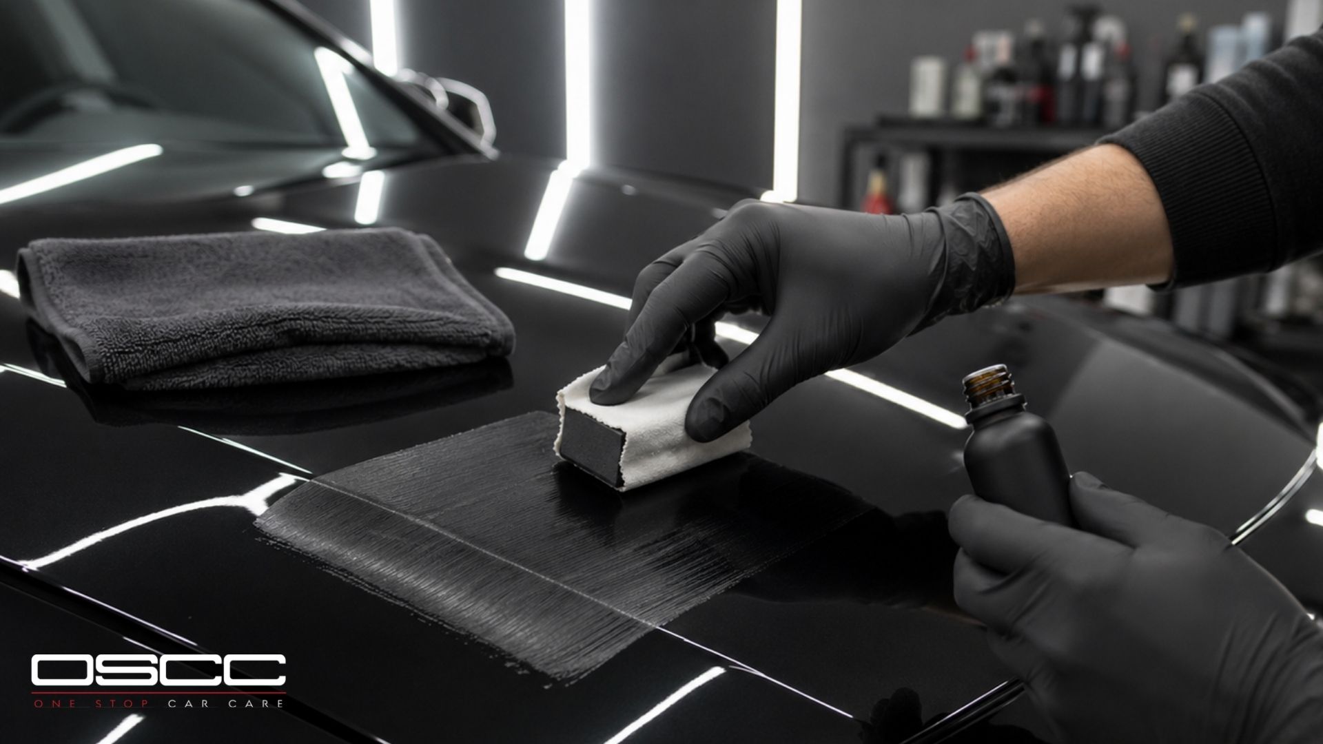 A technician in black gloves applies ceramic coating to a black vehicle hood with an applicator block.