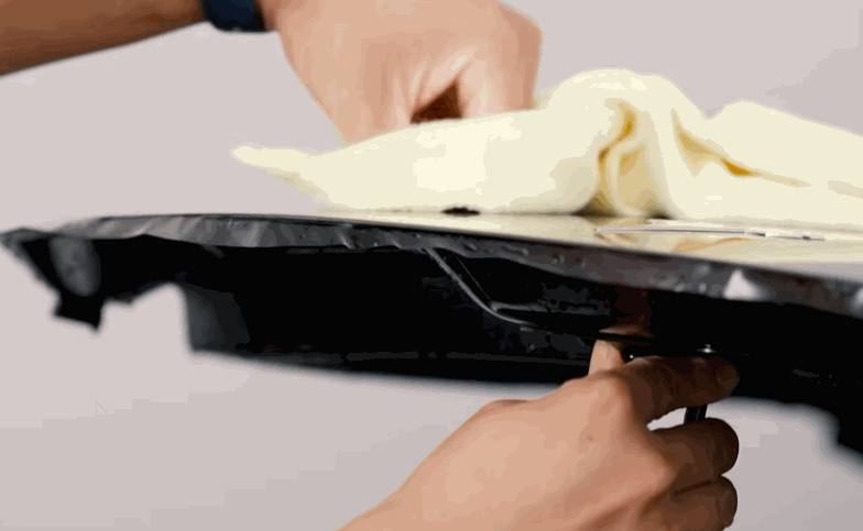 A technician wipes a black vehicle trim piece during paint protection film installation. The close up shows careful prep around the edge before the film is finished.