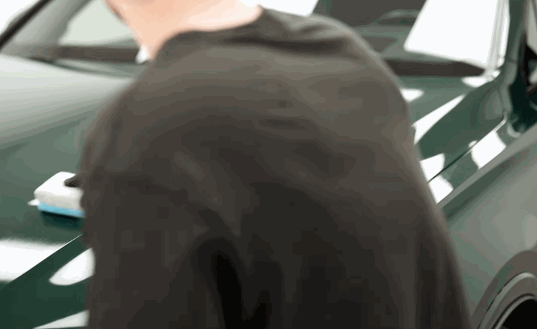 Detailer works on the hood of a green car during ceramic coating preparation.
