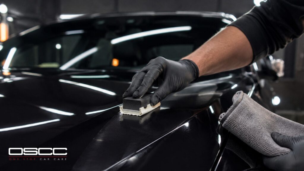 Technician applies ceramic coating to a black car hood with an applicator pad.