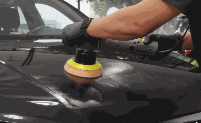 Detailer polishes a black car hood to remove surface haze before ceramic coating.