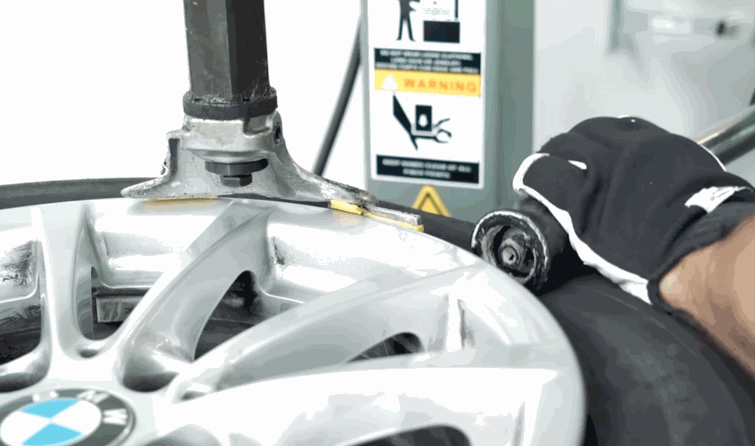 Technician uses a tire installation machine to guide a tire onto a silver BMW wheel.